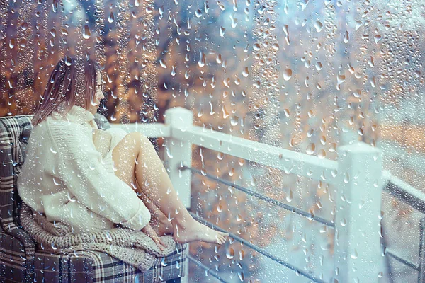 girl with a book in autumn rain on the veranda of the house, seasonal portrait romantic autumn with rain, weather raindrops