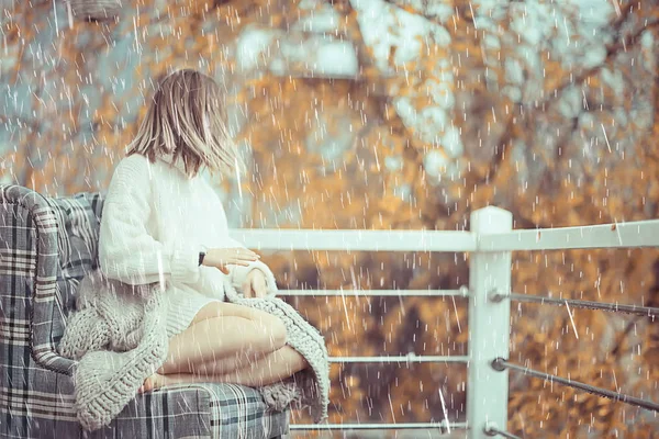 girl with a book in autumn rain on the veranda of the house, seasonal portrait romantic autumn with rain, weather raindrops