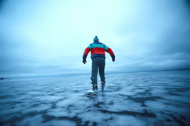 Bir adam donmuş bir gölün buzunda kayıyor, doğa manzarası, açık hava sporları.