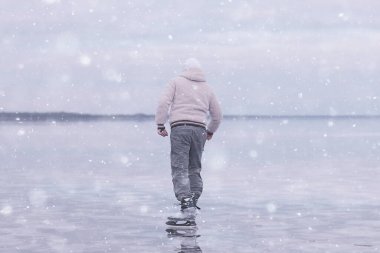 Bir adam donmuş bir gölün buzunda kayıyor, doğa manzarası, açık hava sporları.