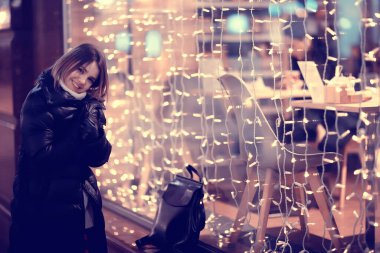 Kız Noel ışıkları akşam dekore edilmiş şehir, şehir dekorasyonları ve çelenklerin arka planında genç bir model, gece şehir ışıkları