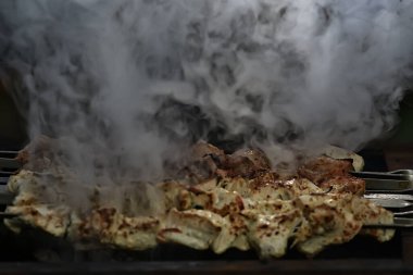 Kömürde barbekü eti, demir şişlerde duman tütsüsü, taze et arka planı.