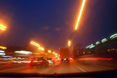 Gece şehrinin soyut görüntüsü bir araba penceresinden bulanık, şehirde trafik...