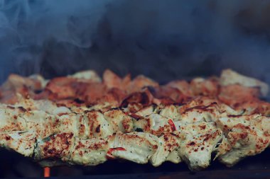 Kömürde barbekü eti, demir şişlerde duman tütsüsü, taze et arka planı.