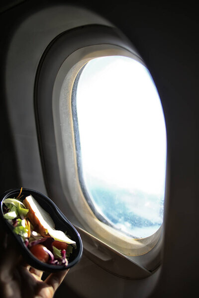 plastic plate container with salad on the background of a window on the plane