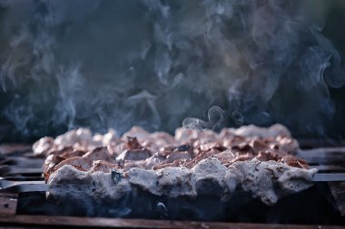 Kömürde barbekü eti, demir şişlerde duman tütsüsü, taze et arka planı.