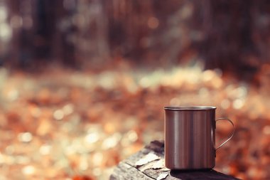 Demir kupa ve sıcak çay. Kamp gezisinde aktif yaşam tarzı. Sonbahar sarı parkı.