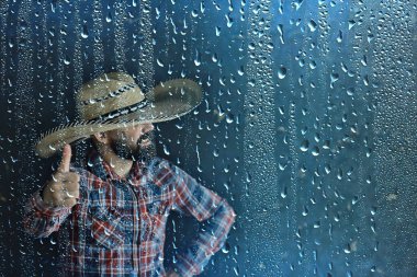 Cam yağmur damlalarının arkasında hasır şapkalı çiftçi, Amerika Vahşi Batı mevsimsel hava durumu