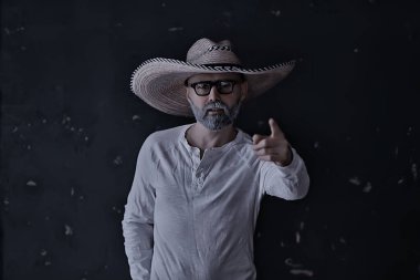 Hasır şapkalı bir adam stüdyoda elleri ve parmaklarıyla işaret ediyor. Batı Amerika Meksika Sambrero tarzı