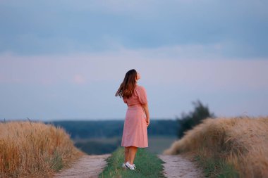 Kadın yazın bir buğday tarlasında yürür, yüzü, yaprakları, ayrılığı olmayan bir arka manzara.