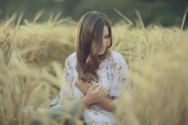 Yazın genç esmer, tarlada uzun saçlı, gün batımında poz veren mutlu insan sağlığı güzeli.