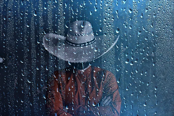 farmer in a straw hat behind glass rain drops, america wild west seasonal weather