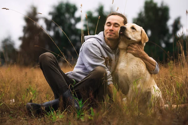 A man sitting with dog in fall field — Stock Photo, Image