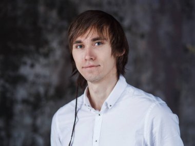 Ayakta ve beyaz bir gömlek gülümseyen yakışıklı kendine güvenen genç bir adam.