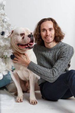 Beyaz arka plan üzerinde hediyeler ile Noel ağacının altında oturan büyük köpek ambul ile mutlu bir gülümseyen adam