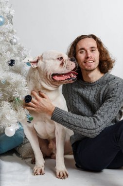 Beyaz arka plan üzerinde hediyeler ile Noel ağacının altında oturan büyük köpek ambul ile mutlu bir gülümseyen adam