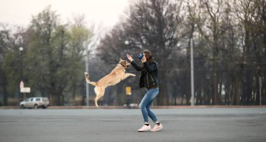 Gün doğumunda meydanda bir kadın köpekle eğleniyor.