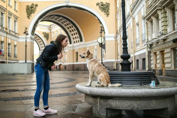 Kobieta spacery z psem wzdłuż ulicy przed fasadą starych budynków w centrum — Zdjęcie stockowe