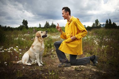 Labrador Retriever 'ın önünde tek dizinin üstünde dururken gülümseyerek gülen rahat genç bir adamın yan görüntüsü
