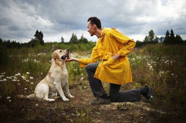 Labrador Retriever 'ın önünde tek dizinin üstünde dururken gülümseyerek gülen rahat genç bir adamın yan görüntüsü