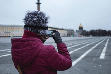 Siyah maskeli genç bir kadının akıllı telefondan ateş edişinin arkası. Şehrin merkezinde kendini izole eden boş sokaklar.