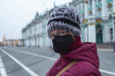 Siyah maskeli genç bir kadın kameraya bakıyor. Şehrin merkezindeki boş dvortsovaya meydanı