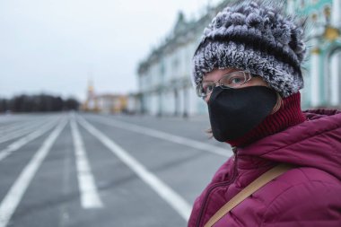 Siyah maskeli genç bir kadın kameraya bakıyor. Şehrin merkezindeki boş dvortsovaya meydanı
