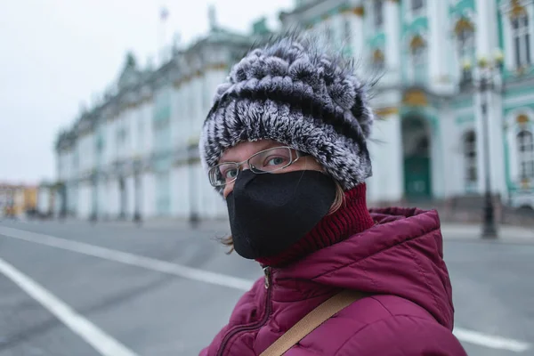 Siyah maskeli genç bir kadın kameraya bakıyor. Şehrin merkezindeki boş dvortsovaya meydanı