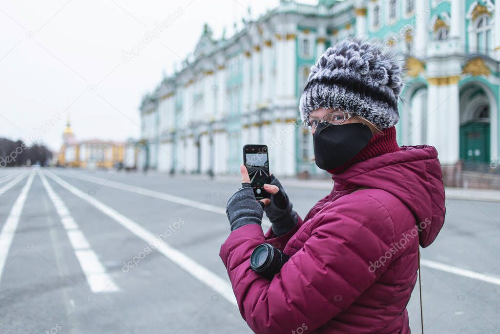 Side view of Young woman in black mask shooting on smartphone Empty streets in the centre of the city on self isolation