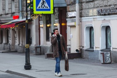 Saint-Petersburg, Rusya - 31 Mart 2020: Genç sakallı adam yolda yürüyor ve telefonla konuşuyor. Kentin merkezindeki boş sokaklar, izolasyonun ilk gününde.
