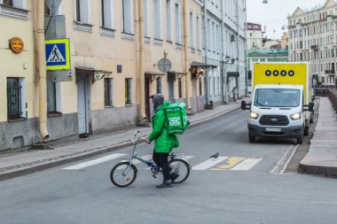Saint-petersburg, Rusya - 31 Mart 2020: Yeşil ceketli ve maskeli kurye, şehirde bisikletle siparişleri teslim ediyor.