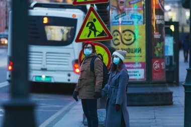 Saint-Petersburg, Rusya - 31 Mart 2020: Maskeli adam ve kadın yol kenarında duruyor ve kaldırımda el ele tutuşuyorlar. Boş bir akşam kenti, alacakaranlıkta kendini izole etmenin ilk gününde..