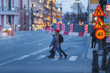 Saint-petersburg, Rusya - 31 Mart 2020: Yaya geçidinden karşıya geçerken kadın ve erkek ellerini maskeliyor. Boş bir akşam kenti, alacakaranlıkta kendini izole etmenin ilk gününde..