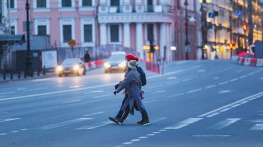 Saint-petersburg, Rusya - 31 Mart 2020: Yaya geçidinden karşıya geçerken kadın ve erkek ellerini maskeliyor. Boş bir akşam kenti, alacakaranlıkta kendini izole etmenin ilk gününde..