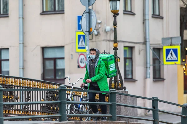 2020年3月31日 ロシア サンクトペテルブルク 緑のジャケットとマスクを着た宅配便が市内を自転車で移動 — ストック写真
