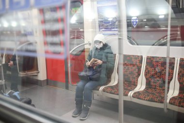 Saint-Petersburg, Rusya - 04 Nisan 2020: Maskeli kadın metroda kitap okuyor. Yeni Coronavirus COVID-19. Salgın veya salgın sırasında sağlık hizmeti kavramı