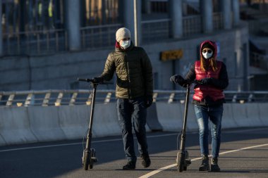 Saint-petersburg, Rusya - 4 Nisan 2020: Elektrikli scooterlı genç bir çift Yakhtenniy Köprüsü 'nde yürüyor. Coronavirüs COVID-19 salgını yüzünden insanlar evde kalıyor..
