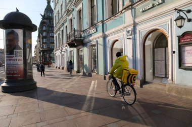 Saint-petersburg, Rusya - 7 Nisan 2020: Nevsky Prospekt. Sırt çantalı sarı ceketli bir yiyecek teslimatçısı kaldırımda bisiklet sürüyor..