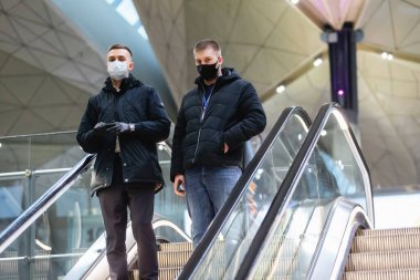 Saint-Petersburg, Rusya, 30 Nisan 2020: Maskeli iki adam Pulkovo Uluslararası Havalimanı 'nın iç kesimindeki kolaylaştırıcıdan aşağı iniyor. Koronavirüs salgını nedeniyle uluslararası uçuşlar iptal edildi.