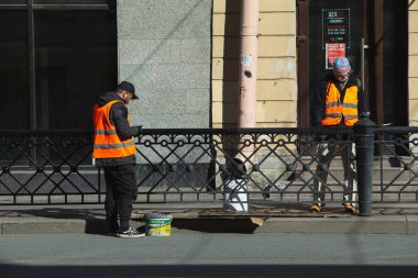 Saint-Petersburg, Rusya - Mayıs 12020: şehir manzarası. Bahar. Ressam caddede çalışıyor. Turuncu üniformalı işçi siyah bir çit boyuyor..