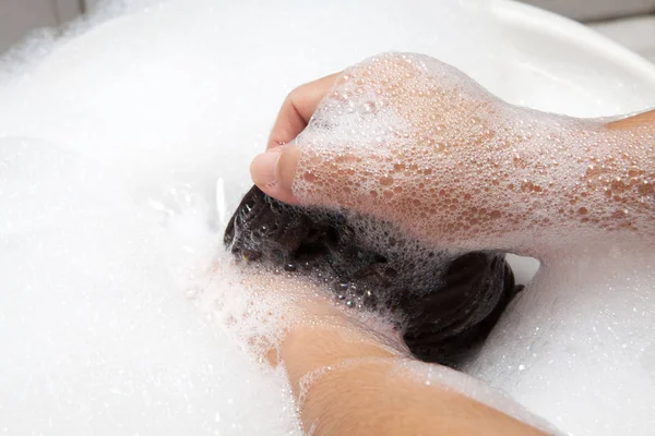 Hand washing clothes with bubble on white basin.