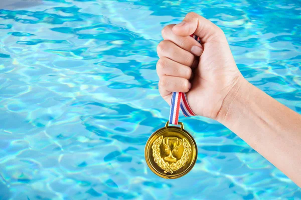 Puñado de hombre asiático sosteniendo medalla de oro con fondo borroso de la piscina . — Foto de Stock