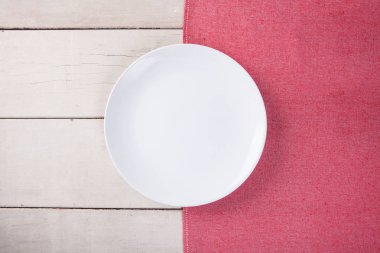 Kırmızı masa örtüsü ve kopyalama yeri olan beyaz ahşap masa boş beyaz plaka üstten görünüm koymak.