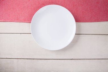 Kırmızı masa örtüsü ve kopyalama yeri olan beyaz ahşap masa boş beyaz plaka üstten görünüm koymak.