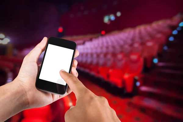 Smartphone en la mano y pantalla blanca con fondo borroso de asiento en el cine . — Foto de Stock