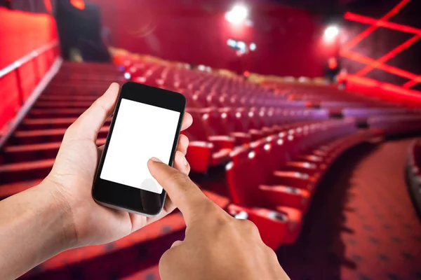 Smartphone en la mano y pantalla blanca con fondo borroso de asiento en el cine . — Foto de Stock