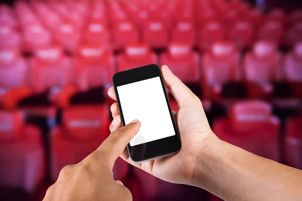 Smartphone en la mano y pantalla blanca con fondo borroso de asiento en el cine . — Foto de Stock