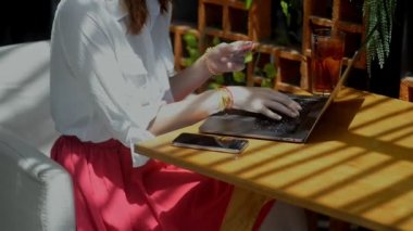 Genç bir kadın internetten alışveriş yapıyor. Yaz terasında dizüstü bilgisayar ve kredi kartı kullanıyor..