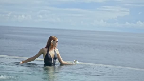 在亚洲的度假游泳池边喝咖啡的年轻美国女人. — 图库视频影像