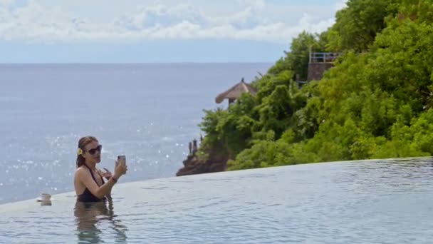 Felice donna americana avendo conversazione utilizzando smartphone alla piscina termale in resort . — Video Stock